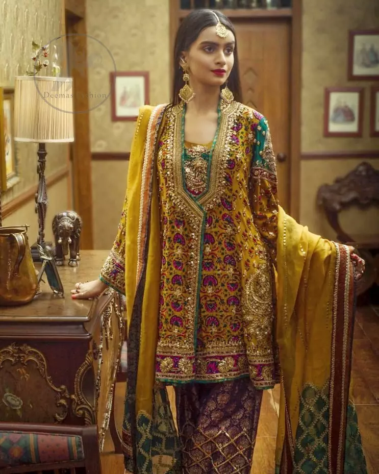 This outstanding angrakha shirt embellished with floral thread embroidery. It is allured with resham, kora dabka, tilla and pearls. Sleeves are decorated with gotta lace and floral embroidery. Embroidered applique on hemline adds to the look. It is beautifully paired up with magenta sharara with gotta criss cross patterns. It comes with chiffon goldenrod dupatta embellished with pea green applique.
