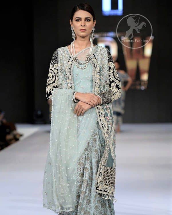 This outfit is a timeless beauty. The blouse is covered with gown embellished with silver gold kora dabka, Sequins and swarovski crystals.This exquisite gown is decorated with embroidered black applique and tassels on hemline.It comes with lehenga style bottom. This Outfit is beautifully coordinated with strip of material that wrapped around the blouse and draped across the front and over one shoulder?