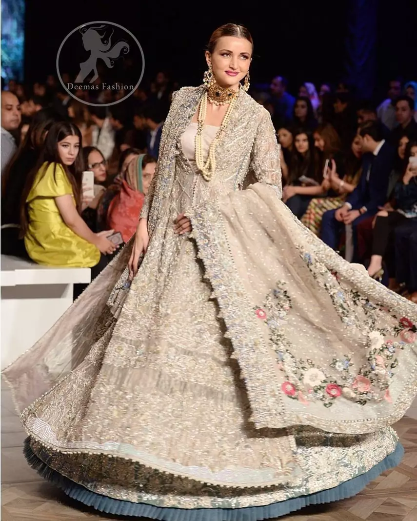 This outfit is a timeless beauty. It is heavily embellished with silver gold kora dabka, Sequins and swarovski crystals. This exquisite Pishwas is fully decorated with floral motifs patterns all over it. It is further enhanced with multiple colored Foral thread embroidery. The applique border of pishwas is ornamented with small silver pearls. It comes with embellished lehenga which has small sized sprinkled floral motifs all over. This Outfit is beautifully coordinated with matching Dupatta with heavy embroidered borders.