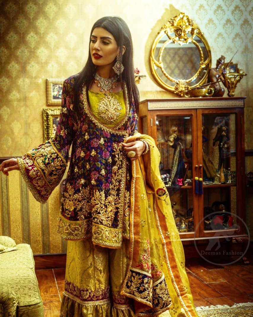 This royal blue angrakha shirt is embellished with resham thread. It is meticulously highlighted with dull golden kora dabka, tilla, sequins and pearls. Sleeves and neckline are adorned with gotta work as well. Hemline is allured with embroidered applique. It comes with embellished gharara which has sprinkled floral motifs. This Outfit is beautifully coordinated with yellow dupatta with heavy embroidered borders.