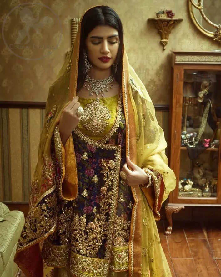 This  royal blue angrakha shirt is embellished with resham thread. It is meticulously highlighted with dull golden kora dabka, tilla,  sequins and pearls. Sleeves and neckline are adorned with gotta work as well. Hemline is allured with embroidered applique. It comes with embellished gharara which has sprinkled floral motifs. This Outfit is beautifully coordinated with yellow dupatta with heavy embroidered borders.