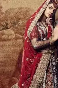 Black floor length net paneled gown is beautifully embellished with silver kora dabka, tilla, pearls and sprinkled sequins all over. It comprises with maroon blouse and skirt. The skirt is ornamented with floral motifs done with silver gold kora dabka, tilla, kundan and sequins work. This outfit is coordinated with maroon dupatta with embroidered borders on all four sides and sequins work on the ground.