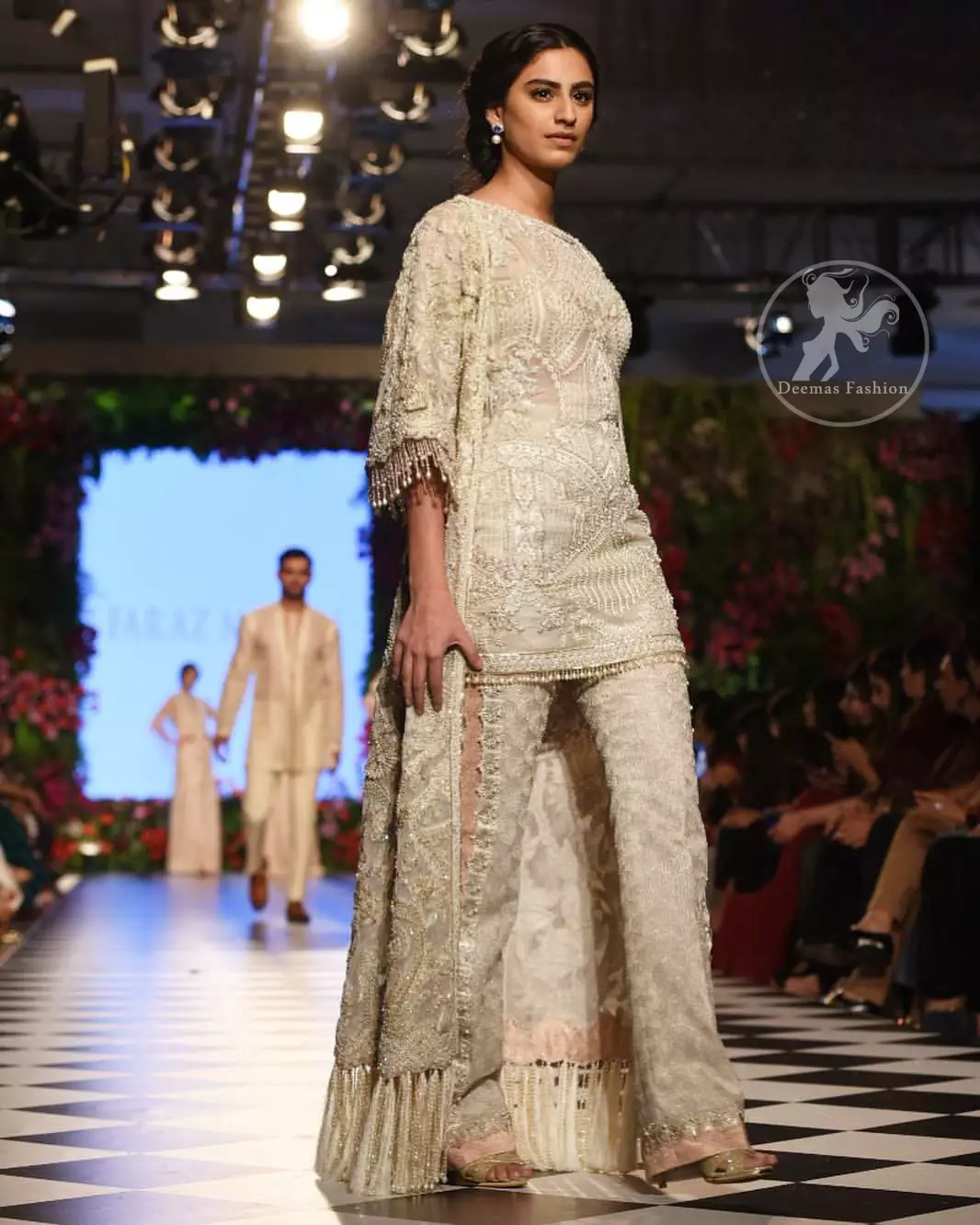Go for this trendy dress. This dress is heavily embellished with floral and geometric styled embroidery decorated with silver kora, dabka, swarovski and pearls. Gown is enhanced with scalloped border decorated with thread clusters finishing. Third quarter sleeves are embellished with floral motifs all over along with tassels at the end. Trousers is magnificently decorated with cutwork. It is coordinated with tissue dupatta which is sprinkled with sequins all over it.