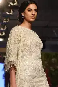 Go for this trendy dress. This dress is heavily embellished with floral and geometric styled embroidery decorated with silver kora, dabka, swarovski and pearls. Gown is enhanced with scalloped border decorated with tassels finishing. Third quarter sleeves are embellished with floral motifs all over along with tassels at the end. Trousers is magnificently decorated with cut-work. It is coordinated with tissue dupatta which is sprinkled with sequins all over it.