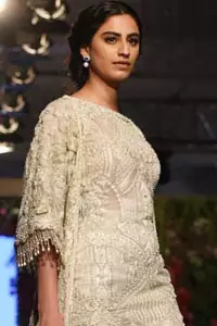 Go for this trendy dress. This dress is heavily embellished with floral and geometric styled embroidery decorated with silver kora, dabka, swarovski and pearls. Gown is enhanced with scalloped border decorated with tassels finishing. Third quarter sleeves are embellished with floral motifs all over along with tassels at the end. Trousers is magnificently decorated with cut-work. It is coordinated with tissue dupatta which is sprinkled with sequins all over it.