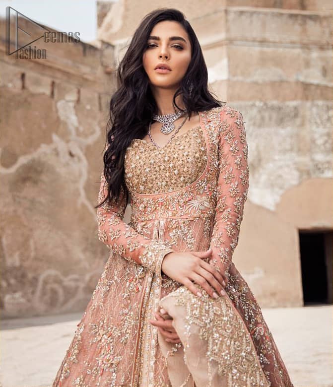 This garnet ensemble is sure to make you look like glamorous royalty with immaculate work covering every inch of the frock. The bodice of the frock is heavily embroidered with champagne zardozi work. Furthermore the hemline is ornamented with geometric patterns. It is coordinated with peach and light pink lehenga with a flowing train embellished with light golden and champagne embroidery and scattered floral motifs in a sequence.  this is an ensemble that deserves to be flaunted. Style it up with light pink dupatta having four sided embroidered border.