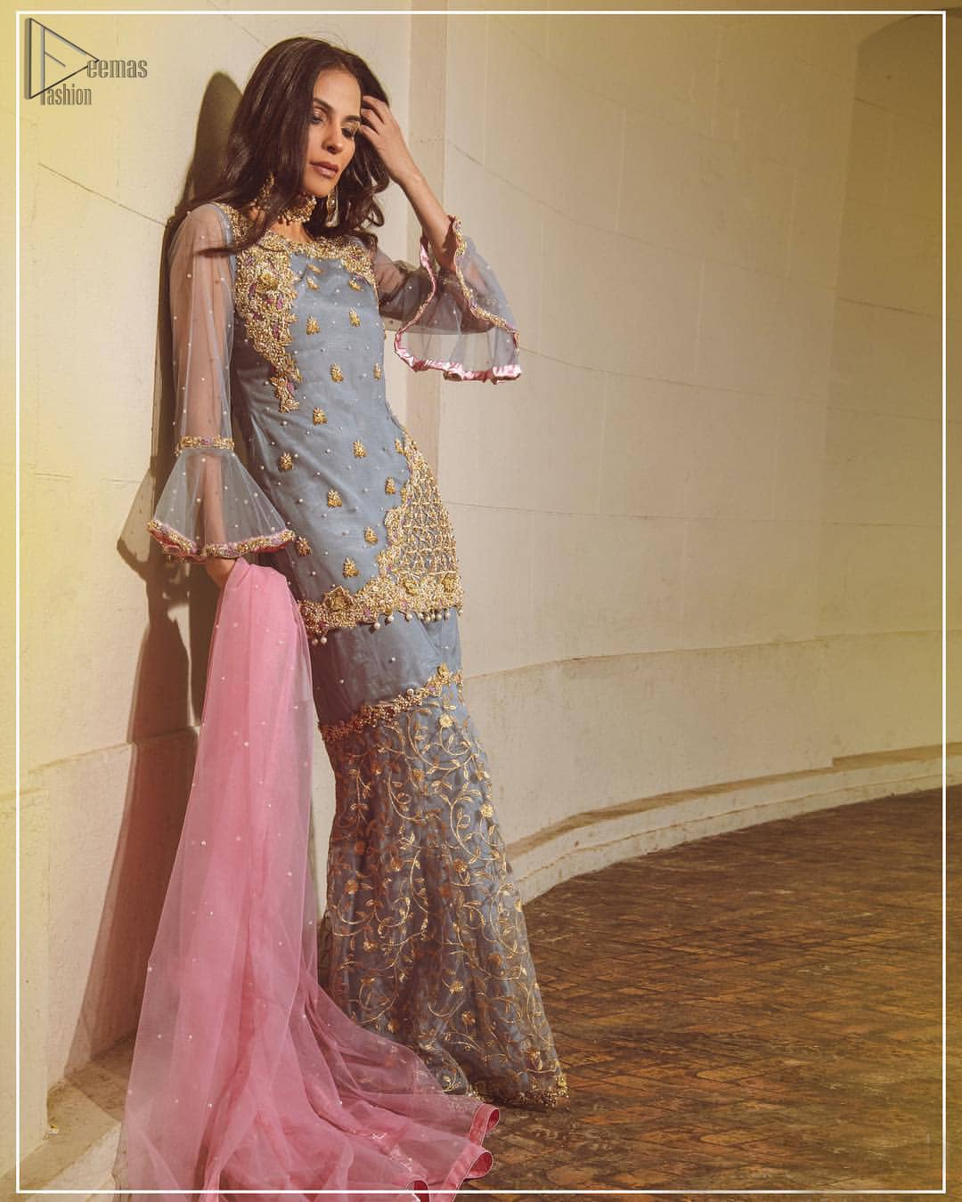Embrace the season of festivities with this beautiful dress. The chic yet elegant outfit is decorated with golden embroidery, embellished neckline and tiny floral motifs. Borders are even more enhanced with golden zardozi detailed patterns and finished with scallops and dangling balls. Pair it up with gray sharara highlighted with floral jaal and scalloped bottom done with golden kora, dabka and tilla work. The look is complete with pink net dupatta sprinkled with sequins all over.