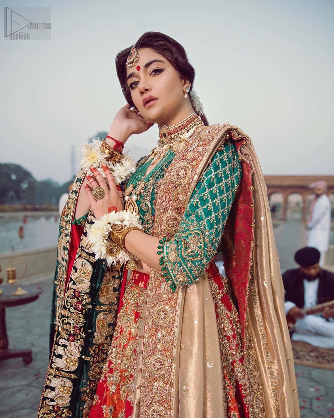 Classic, timeless and truly beautiful, our bridal dress is perfect for your unforgettable day. Excellence of craftsmanship is evident with intricate detailing that features the use of zardozi work. The blouse is beautifully adorned with geometric patterns and floral embroidery with golden zardozi work and finished with dangling beads. Complete the look with artfully coordinated lehenga which is ornamented with a bold and captivating design with a traditional intricate embroidery and scattered tiny floral motifs. The combination of red and orange for lehenga is also captivating. Elegance is personified when it gets paired up with golden dupatta having four sided embroidered border.