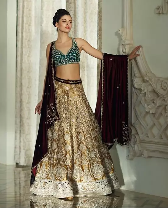 Delicately crafted and personifying chic elegance with an element of grandiose. Gussy up in this luxuriously designed lehenga blouse emboldened with intricate embroidery along with beautiful rich patterns and delicate details at the bottom. The maroon waist belt on lehenga make it so classy. It comprises with teel blouse adorned with tiny floral motifs in the shade of silver. The outfit is pair up with maroon velvet dupatta emphasized with silver and golden zardozi work on all four sides.