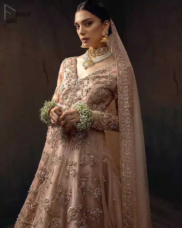 Pictured in a fabulous outfit, Chic and sophisticated perfectly describe this simply stunning wedding dress. The shirt is meticulously embellished with antique brass zardozi work. The sequinned whimsical florals embroidered across the flattering bodice in this ethereal gown is sure to turn heads in every room you walk into. Balance the look with a tea rose tissue lehenga. Pair it up with an organza dupatta which is sprayed with sequins glorifying its grace. Moreover, it is also enhanced with a four-sided embellished border that increases the enormous adornment of the whole outfit.