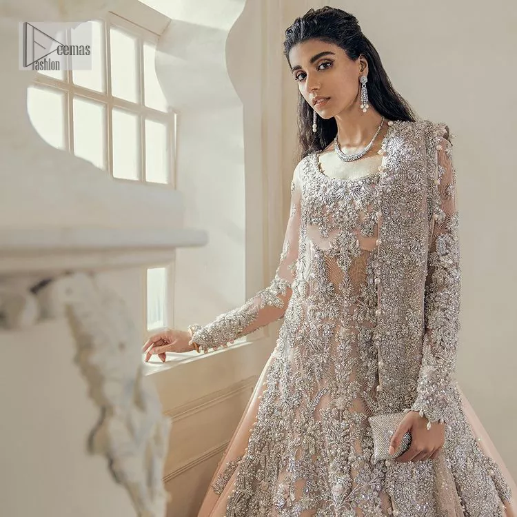 Get yourself a sweet treat, as this ensemble showcases the majestic light orange colour inscribed with lustrous embellishments. A combination of light orange attached grantly to the organza scalloped shirt heightened with silver embroidery. The shirt is intensified with tones of dabka, tilla, kora and blossoms of Resham coupled with a defined sweetheart neckline along with full sleeves. It is coordinated with a flared sharara which is embellished with floral motifs and ornamented borders. This outfit establishes a vibe of its own on your Walima day when finished with a dupatta which is framed with four-sided borders and sequins sprayed all over.