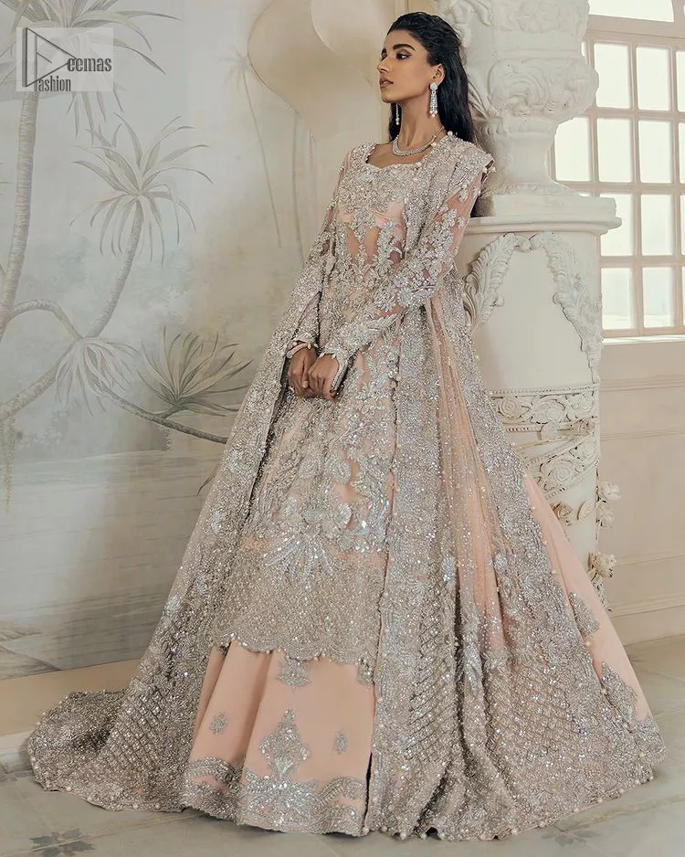 Get yourself a sweet treat, as this ensemble showcases the majestic light orange colour inscribed with lustrous embellishments. A combination of light orange attached grantly to the organza scalloped shirt heightened with silver embroidery. The shirt is intensified with tones of dabka, tilla, kora and blossoms of Resham coupled with a defined sweetheart neckline along with full sleeves. It is coordinated with a flared sharara which is embellished with floral motifs and ornamented borders. This outfit establishes a vibe of its own on your Walima day when finished with a dupatta which is framed with four-sided borders and sequins sprayed all over.