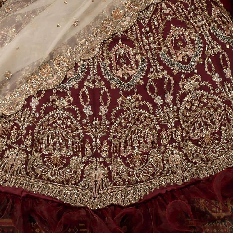 Take your style up a few notches in this elegant reception piece. A pure organza maroon fluffy lehnga is beautifully hand-rendered with golden embroidery and enhanced with  tilla, sitara, pearls, dabka and zardozi work. It is paired up with a blouse choli with tilla motifs on the full sleeves along with boat shape neckline to make your Big day astonishing and remarkable. The ivory organza dupatta has a four-sided embroidery adorned with pearls and Sitara and is framed with a scalloped style.