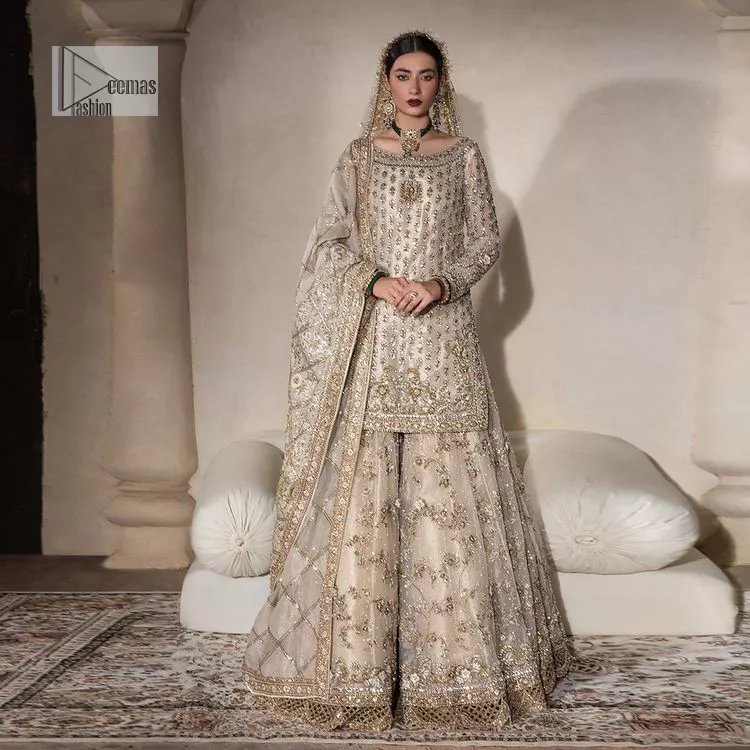 Unravel your inner density with our ivory nikah outfit. DeemasFashion presents this outfit which is embellished with light golden embroidery that further intensifies with tilla, dabka, kora, Kundan and the real magic of Zardozi. The ivory short shirt has boat shape neckline that is the epitome of royalty and grace. In addition to this, the embellished full sleeves also give a stunning touch to the shirt. It is coordinated with scalloped sharara making it a perfect choice to pair with the short shirt. Finish this outfit with a dupatta framed with four-sided embellished borders that gives you an impressive appearance on the Big day.