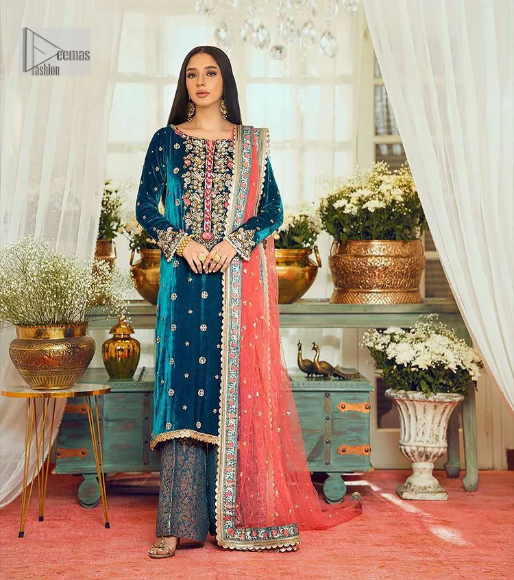 This dazzling yet elegant ensemble is perfect to make a statement at any event.  Long shirt for party dress in teal blue colour is embellished with multiple colour embroidery which is prominent with dabka, naqshi, stones, tilla, crystals work. The boat shape neckline is decorated with embroidery and with full-length sleeves. The fabric used for the shirt is velvet. It is paired with jamawar trousers in the same colour that is unique in style. Finish this party wear with a scalloped dupatta framed with a four-sided border and ting floral motifs all over that is the perfect choice for a party.