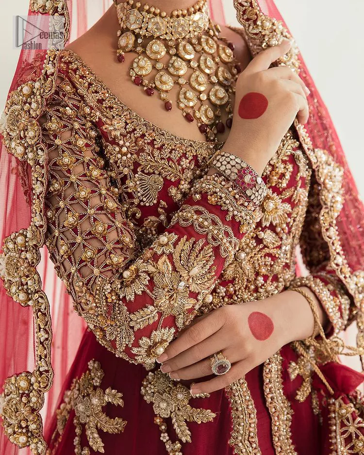 Be a dreamy vision in this reception wear. The beautiful pishwas in the bright red shade is embellished with intricate designs and fine details. It is enhanced with hand-crafted golden embroidery with details of tilla, dabka, kora, Kundan and magic of Zardozi. The round neckline and three-quarter sleeves feature a heavily crafted geometric pattern enhanced by cutwork detailing. The following front open scalloped pishwas is organized with a back train lehenga whose border is beautifully decorated with embroidery making it an epitome of beauty and grace. Furthermore, The embellished borders of the red scalloped dupatta give a perfectly glamorous look to the beautiful overall outfit. It is also intensified with sequins spray.