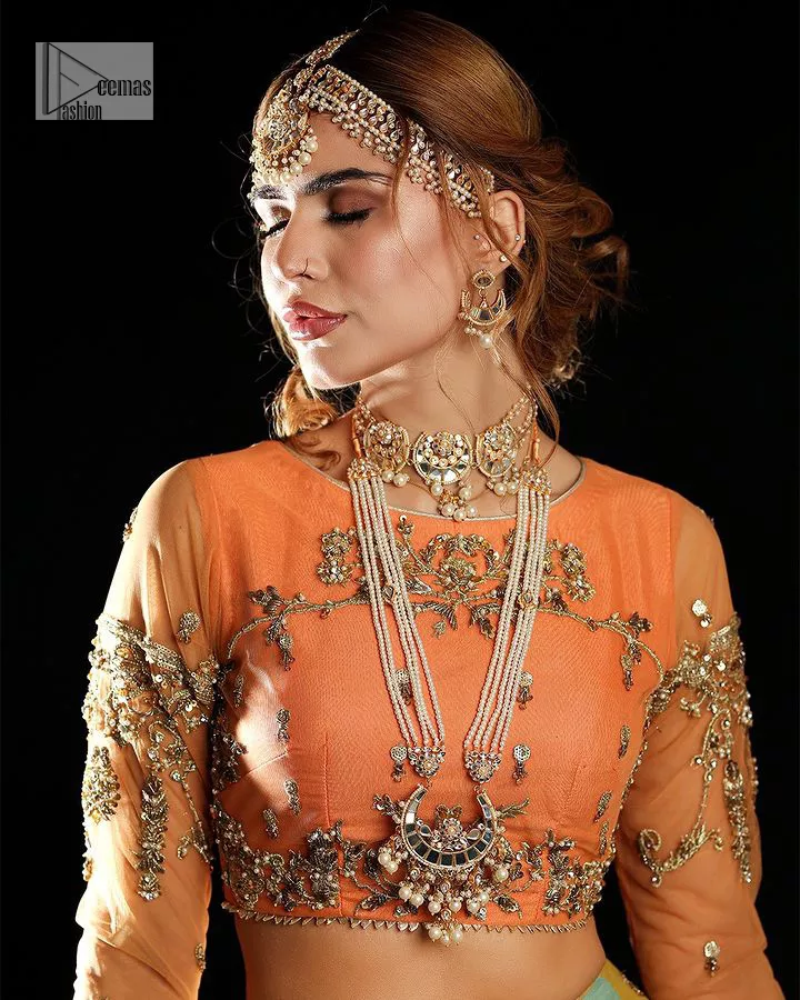 Fun colours, fresh you.  This breathtaking blouse in light orange colour is gracefully adorned with hand-crafted embellishments and lavish golden work creating a magnificent masterpiece to give you your desired appearance. The boat shape neckline of the mehndi wear is the epitome of beauty. Further, the embellished three-quarter is adorned with lavish designs and fine details making it a perfect choice to pair with the lehenga. It is organized with lehenga having multi-colour panels to give you a fresh and rainbow look on your mehndi. The lehenga is also adorned with tilla, dabka, kora, Kundan and the real magic of Zardozi. Complete this article with a dupatta, framed with four-sided borders and floral motifs on pallu to make your day Funday.