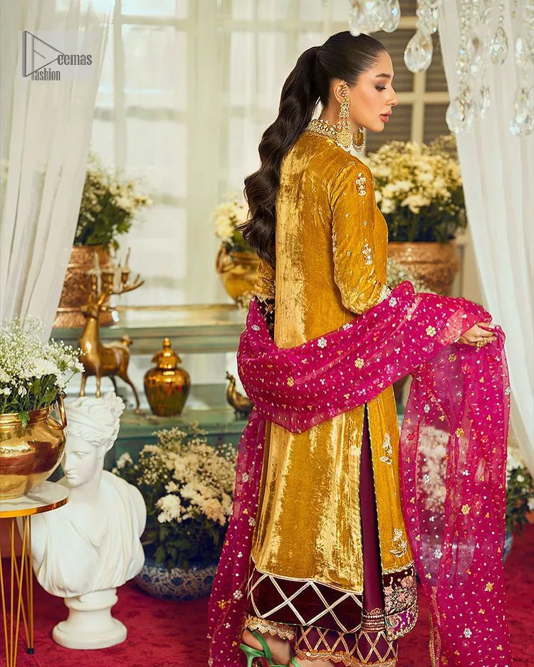 This mustard ensemble features zari and tilla details creating the perfect magical look for the season! The stunning long shirt in an alluring mustard shade comes in velvet fabric. The V-neckline of this shirt is emblazoned with embroidery and hand-crafted embellishments. Motifs, tilla, and threads give a perfect finishing look to the shirt. It is enhanced with multiple colours embroidered patches at the bottom to stole everyone's heart. It is paired with scalloped burgundy trousers to balance the overall look of this party wear. Complete this with a dupatta having tiny floral motifs and sequins sprayed all over.