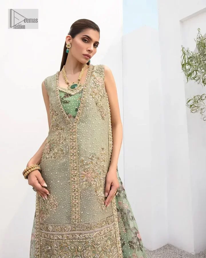 The timelessly classic mint green nikah outfit! The beautiful model looks ravishing in this mint green shirt, heavily hand-embellished with floral motifs and sequins spray. The back of the shirt is sprayed with sequins and has an embellished border; an embellished front and back panel border makes this outfit unique. The V shape neckline adds super beauty to the outfit which involves tilla, dabka, kora, Kundan and the real magic of crystals. Further, the sleeveless style is for extra comfort zone. It is paired with a flared lehenga with an intricately embellished border. 