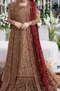 The copper long shirt is paired with a farshi-style lehenga and a maroon organza dupatta to create a traditional look. The shirt is made from pure tissue, which gives it a soft metallic finish that works well with antique embroidery spread across the front and sleeves. Its round neckline and full sleeves let the colour and craftsmanship stand out